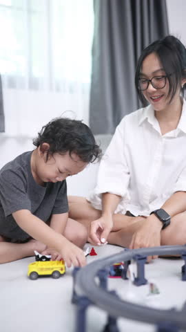 Mother and son enjoying quality playtime with toy trains at home, sharing smiles and a joyful moment in a cozy white room.