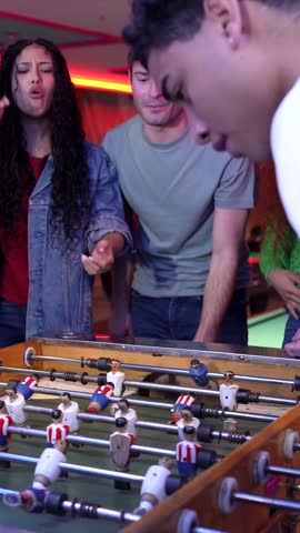 Friends engaging in energetic foosball competition, laughing and enjoying gameplay inside vibrant arcade setting with playful social interaction