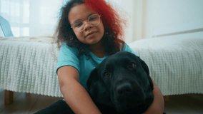 Young girl tenderly hugging black Labrador, sharing warm moment of affection while sitting on bedroom floor near bed, expressing deep bond between child and pet - Powered by Shutterstock - Get 15% off with code: PIKWIZARD15