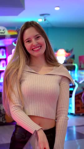 Cheerful young woman smiles while colorful lights change behind her in a vibrant arcade setting