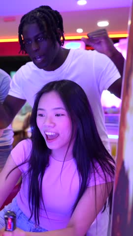 Group of diverse friends competing and cheering during exciting motorcycle racing game at vibrant bowling alley, sharing joyful moment of leisure and togetherness