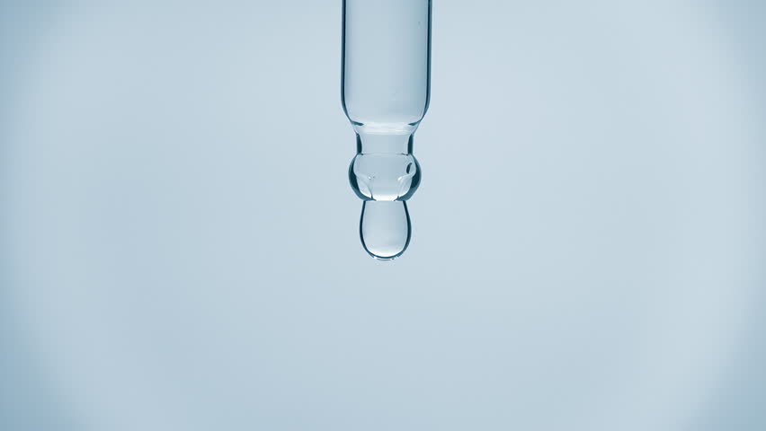 Cosmetics blue liquid dripping from laboratory glass pipette in super slow motion. Macro shot of drop hanging down from chemical dropper. Abstract body care serum ingredients formulating concept