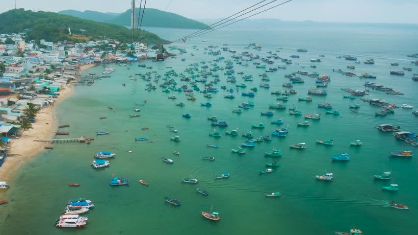 Longest cable car ride in the world on Phu Quoc island, Vietnam with fishermen boats anchored in turquoise sea and coastal fishing village below. Modern Hon Thom cable car cabin. Aerial view