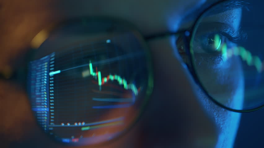 Trader wearing glasses is working on laptop computer. Screen with stock market charts and Bitcoin BTC or Ethereum ETH data analysis reflection. Broker trading online. Altcoins crypto currency trading