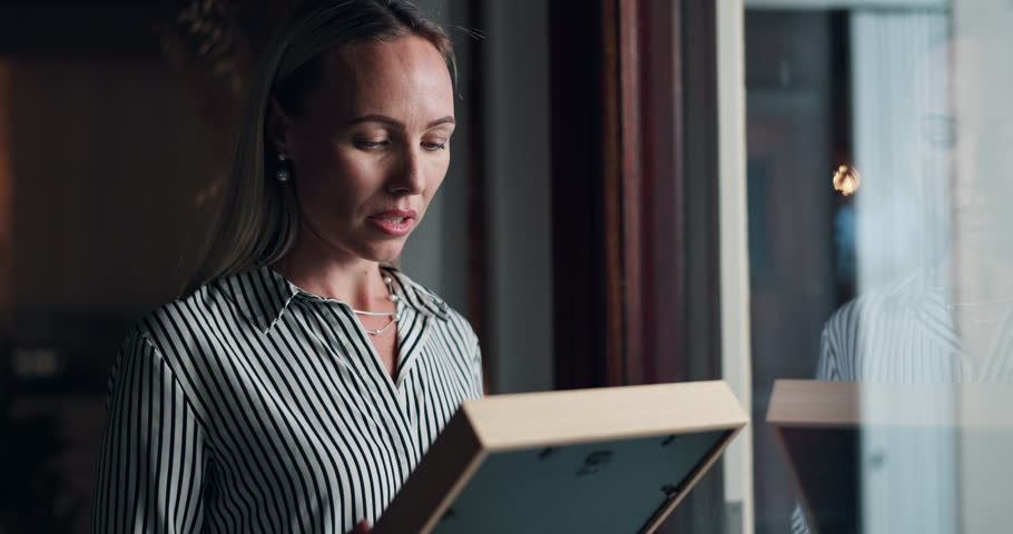 Woman, picture and sad by window at home with memory, mourning and regret or loss of loved one. Female person, widow and hug photo frame with sorrow at house with nostalgia, lonely and reflection