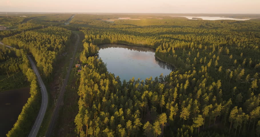 Aerial view around a mirroring forest pond, sunny, summer morning in the Nordics