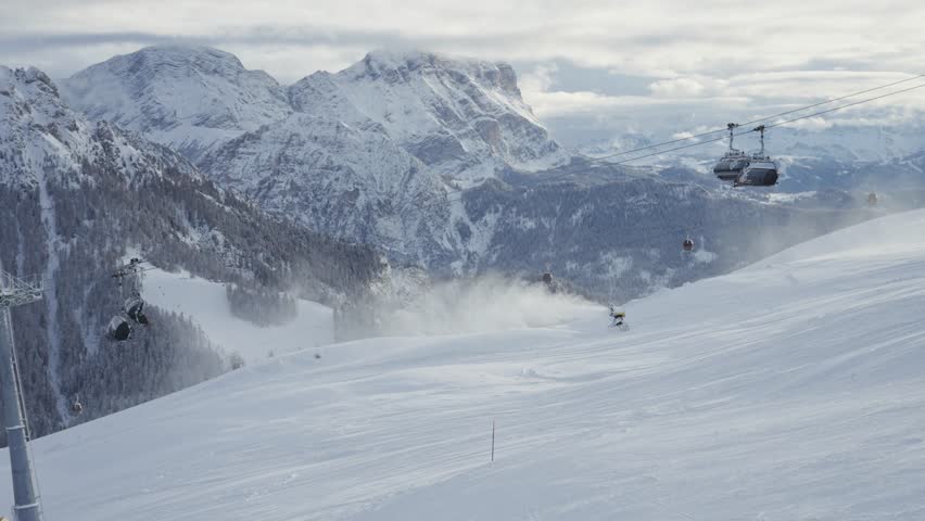 A scenic view of a ski lift carrying passengers over a winter landscape with high mountain ridges in the Italian Alps. Parallax video.