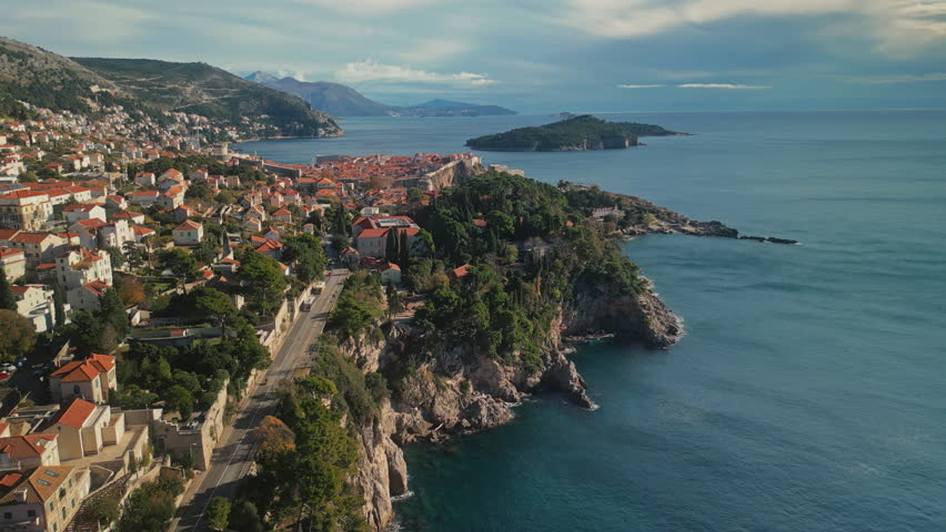 Medieval touristic place Dubrovnik town and freeway on cliffy coast at twilight camera moving forward. Breathtaking landscape with ancient city and mountains and harbor aerial view
