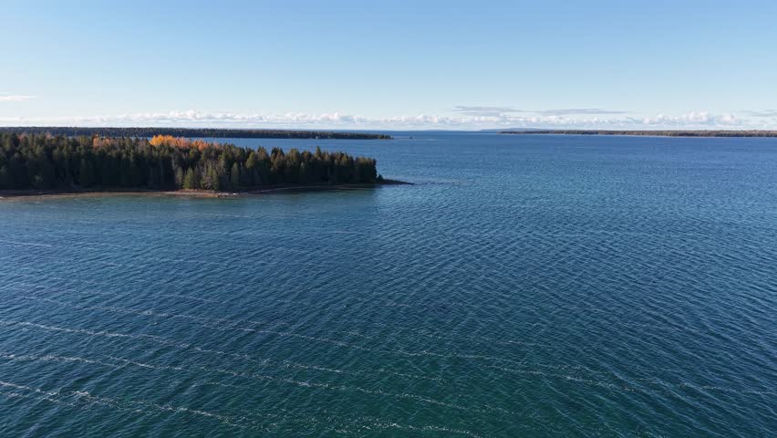 Crisp aerial view over deep blue Lake Superior with a distant wooded shoreline under clear skies