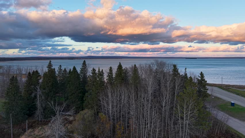 Aerial view of pine forest meeting Lake Superior shoreline under a dramatic evening sky in Michigan’s Upper Peninsula