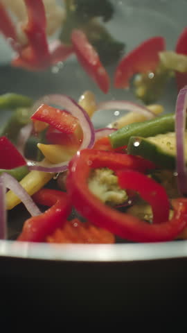 Closeup of chef preparing and throwing vegetable mix on frying pan. Preparation fresh appetizing food. Vegetables flying in slow motion. Healthy vegetarian food cooking. Vertical video