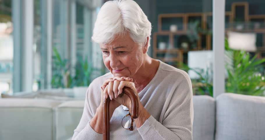 Thinking, sad and senior woman with stick in living room of retirement home with dementia. Mental health, alzheimer or lonely elderly female person with disability, memory nostalgia or depression