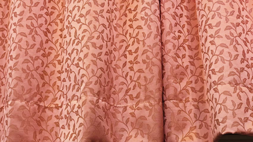 Close-up of peach colored curtain with foliate pattern moving on wind.