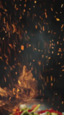 Closeup of chef preparing and throwing vegetable mix on frying pan on fire. Preparation fresh appetizing food. Vegetables flying in slow motion. Healthy vegetarian food cooking. Vertical video