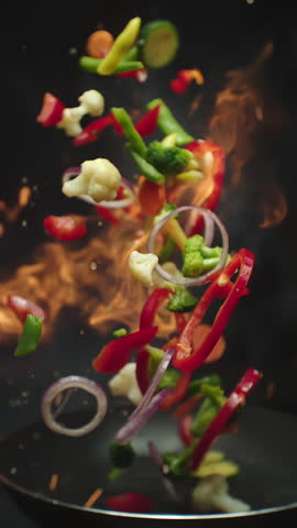 Closeup of chef preparing and throwing vegetable mix on frying pan on fire. Preparation fresh appetizing food. Vegetables flying in slow motion. Healthy vegetarian food cooking. Vertical video