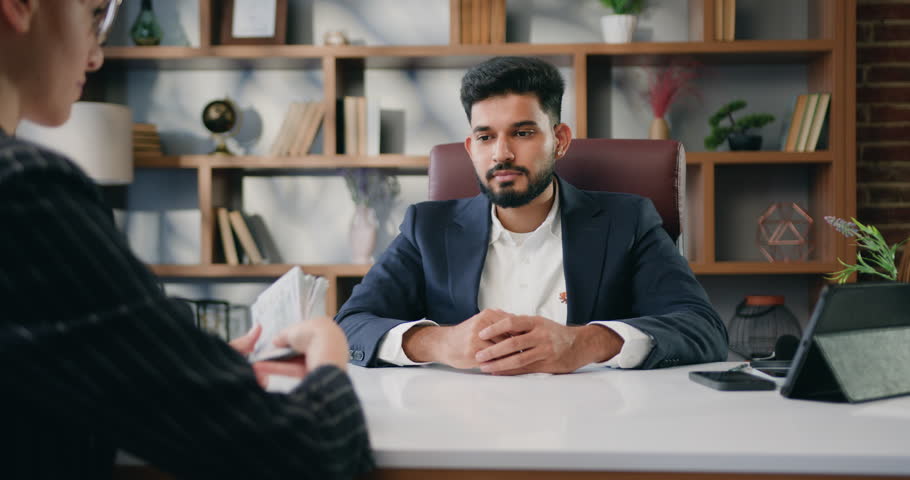 Business man receiving money from colleague in remote workplace. Business man and woman sitting at table and counting money. Woman giving pack of cash to man worker.