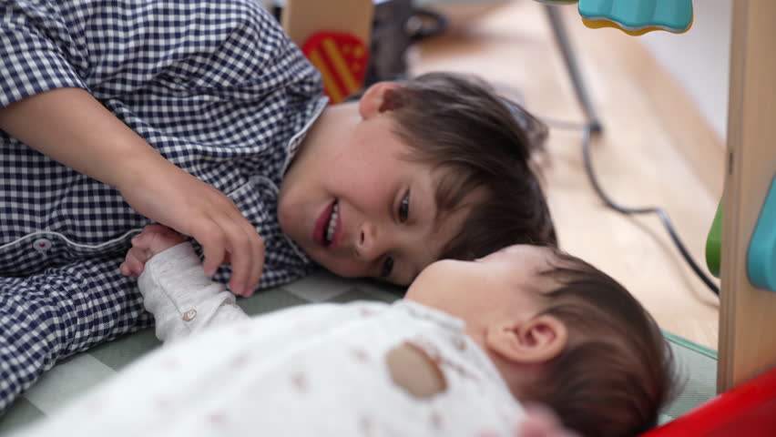 Close-up of a young boy and baby sibling lying on a checkered mat, creating a heartwarming scene of sibling connection, affection, and family love