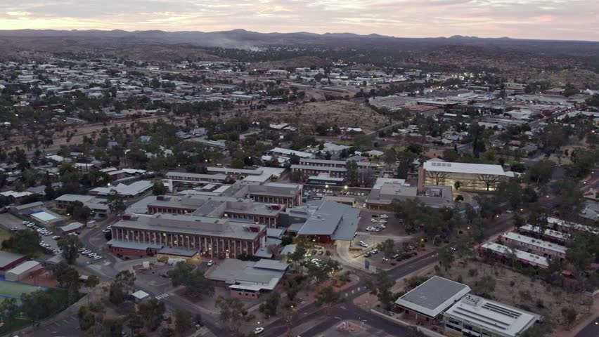 Sideways aerial footage of the township of Alice springs, Mparntwe, including the Alice Springs Hospital, at dusk, in the Northern Territory, Australia. August 2022.