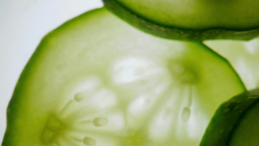 Vegetable colorful pattern background. Macro shot of fresh juicy green cucumber slices moving against skylight, showing flesh and seeds with watery structure texture of vegetable visible under light.