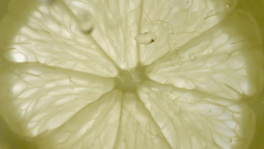 Drops of liquid falling on fresh sliced lemon pieces in slow motion. Beautiful ice water splash on lemon slices in macro. Vitamin C or serum acid in cosmetic product