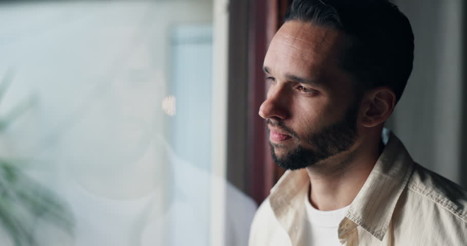 Depression, thinking and window with man at home for mental health, memory and psychology. Mistake, fear and loneliness with male person in living room of house for sad, grief and reflection