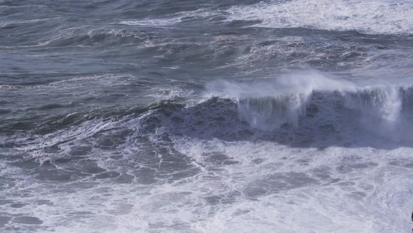 Massive ocean waves surging, cresting, and dramatically breaking along rugged coastline of nazare, portugal, revealing powerful maritime energy and iconic surfing destination