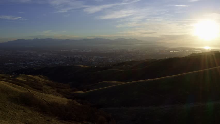 Extreme wide aerial drone shot over the green rolling hills of the bonneville shoreline trail next to Salt Lake City, Utah during a beautiful golden sunset in spring
