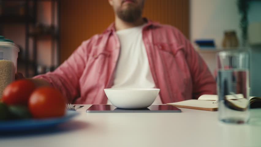 Plus-size man weighing food portions on scale, counting calories for weight loss