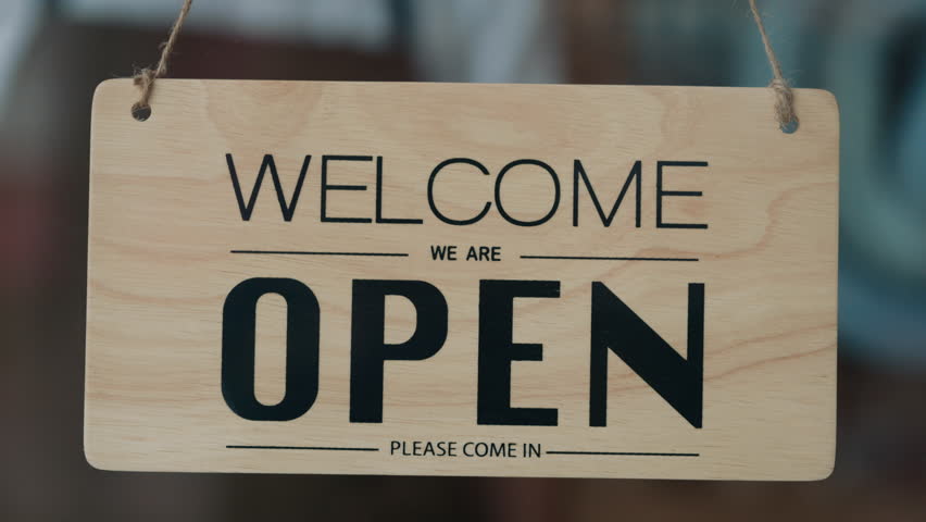 Closeup view of worker hands turning sign Open to Sorry We are Closed on glass door. Skilled waiter in uniform informs guests about coffee shop work ending. Restaurant service