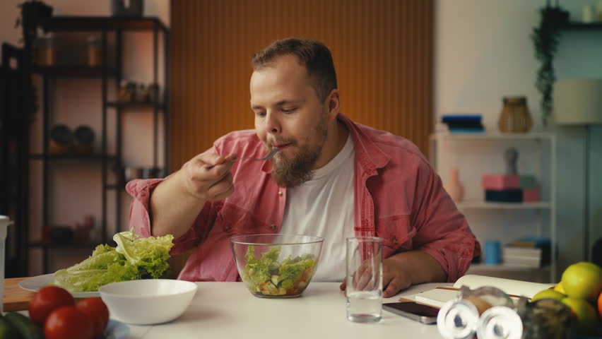 Plus-size man eating salad, motivated to lose weight through healthy dieting