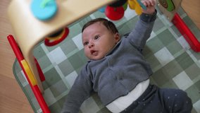 Baby playing on an activity mat, reaching up to interact with colorful toys. The playful setting highlights the baby’s curiosity and early development in a nurturing environment - Powered by Shutterstock - Get 15% off with code: PIKWIZARD15