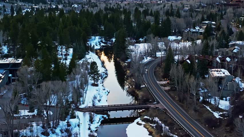 Glacial river winds between snowy pine ridges as low sun casts soft shadows across forest winding through Aspen Colorado