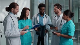 Group of five multiethnic medical students interns men women doctors analyzing patient x-ray result using digital tablet writing clipboard consulting discuss health treatment inside hospital hallway - Powered by Shutterstock - Get 15% off with code: PIKWIZARD15