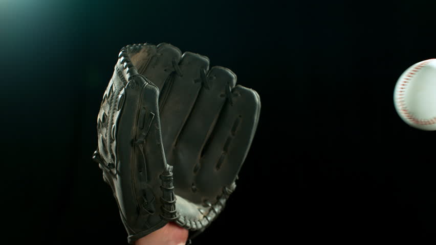 Super slow motion of hand in brown leather baseball glove caught ball isolated on black background . Filmed on high speed cinematic camera