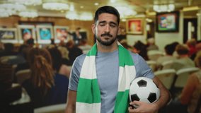 Young man holding soccer ball wearing scarf stands in crowded art gallery observing exhibition indoors looking thoughtful with artistic ambiance around. - Powered by Shutterstock - Get 15% off with code: PIKWIZARD15