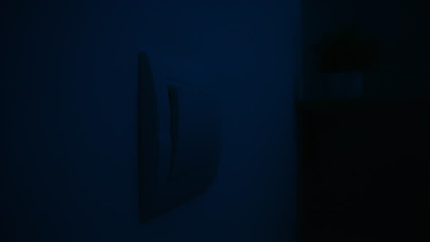 A person is pressing a light switch on a wall to turn on the lights, illustrating energy saving actions. Close up, slow motion