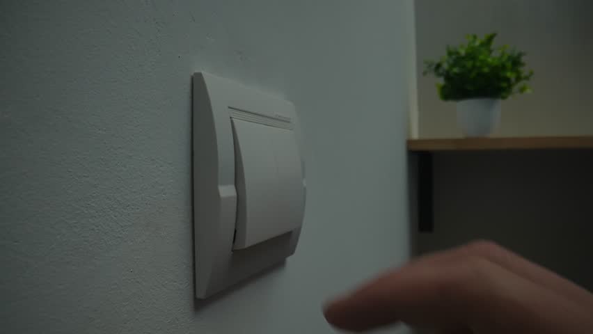 A person is pressing a light switch on a wall to turn on the lights, illustrating energy saving actions. Close up, slow motion