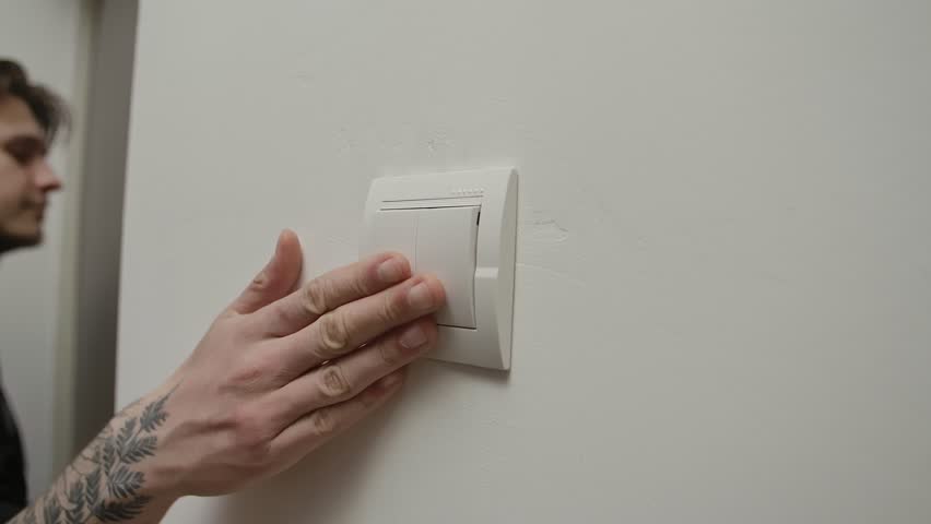 A hand reaches to turn off a light switch in a dimly lit room, bathed in a calming blue hue. Close up, slow motion