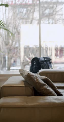 Comfortable leather sofa with pillows in a modern showroom. The large window offers a blurred view of the street outside. Natural light illuminates the furniture, elegant design and inviting ambiance.