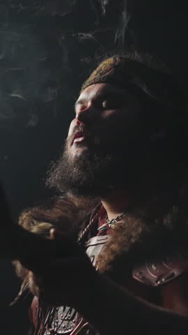 Ecstatic young shaman in Altai ethnic costume and swirling smoke on dark background slow motion. Spiritual traditions of Siberian folks