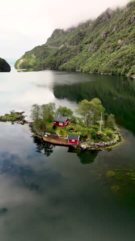 A beautiful cabin nestled on a small island reflects in the calm waters of a Norwegian fjord. Lovrafjorden Norway