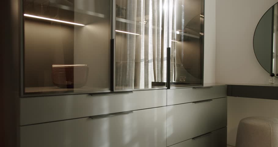 Modern walk-in closet with glass doors and integrated lighting. Stylish storage solutions for clothes and accessories. The wardrobe interior is neatly arranged.