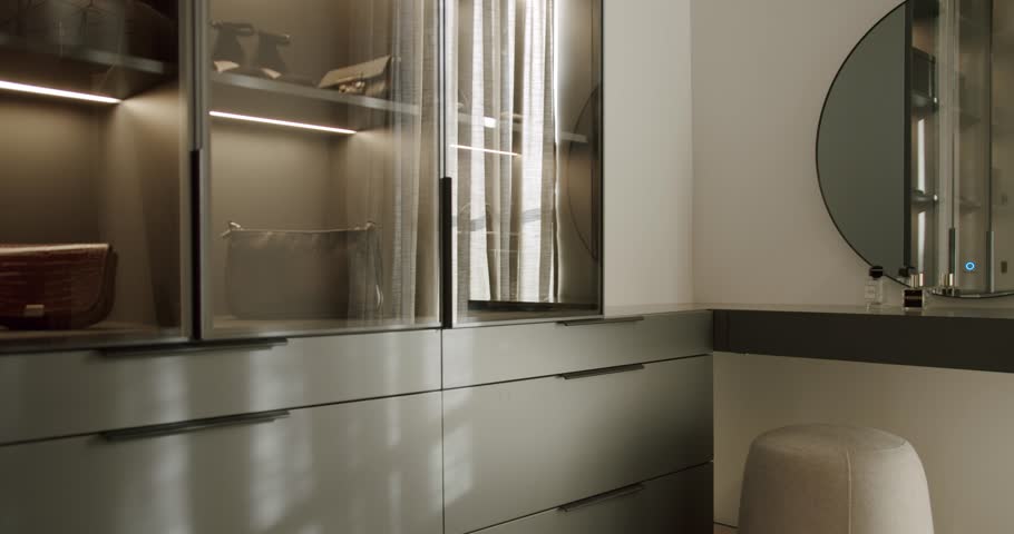 Modern walk-in closet with glass doors and integrated lighting. Stylish storage solutions for clothes and accessories. The wardrobe interior is neatly arranged.