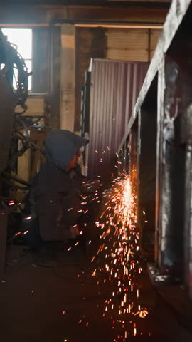 Bright hot sparks fly by welded steel frame in manufacturing plant workshop closeup. Flame torch on caused metal details connected welding machine