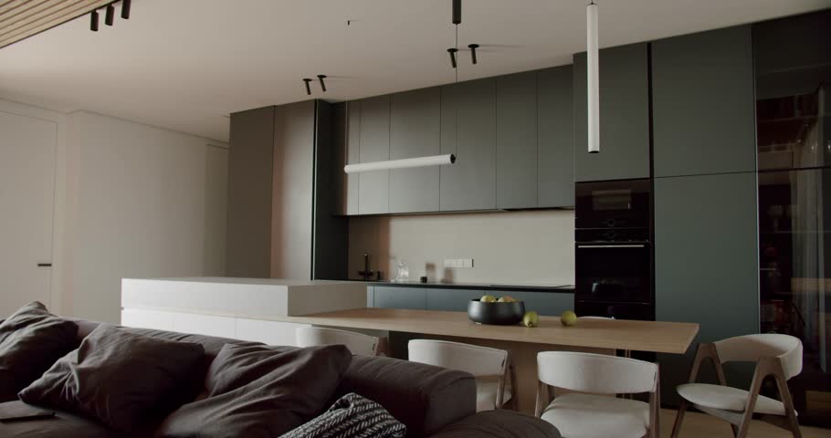 Modern open plan kitchen and living room interior. Comfortable sofa, natural wood dining table and chairs, stylish lamps, and sleek kitchen cabinets. Minimalist, spacious, and inviting.