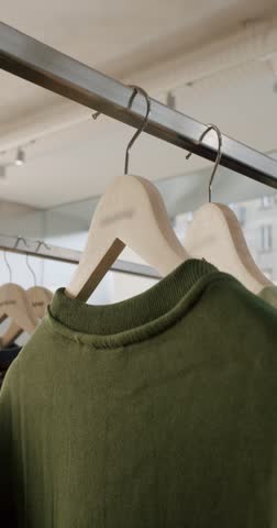 Close-up of various colorful t-shirts hanging on wooden hangers in a clothing store. The camera focuses on the details of the shirts and hangers, showcasing the store