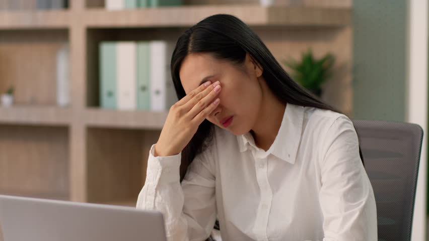 Thoughtful suffering sad Asian Japanese office worker manager business woman Chinese Korean female businesswoman entrepreneur working laptop suffer headache holding head eyestrain pain dry eye indoor