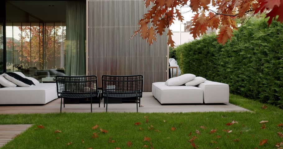 Modern backyard patio with comfortable seating, a lush green lawn, and autumn leaves scattered around. The warm, inviting scene evokes feelings of relaxation and tranquility.
