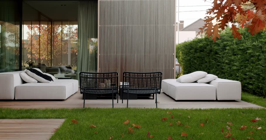 Modern backyard patio with comfortable seating, a lush green lawn, and autumn leaves scattered around. The warm, inviting scene evokes feelings of relaxation and tranquility.