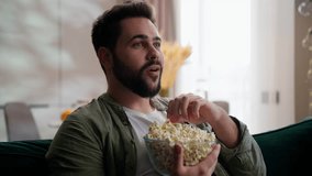 Happy relaxed Caucasian bearded model business man male guy businessman homeowner client sitting sofa at home eating snack popcorn bowl watching TV television series using remote controller film movie - Powered by Shutterstock - Get 15% off with code: PIKWIZARD15